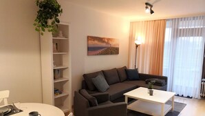 Een woonkamer met een bank, salontafel en een eettafel gedekt voor twee personen. Er is een boekenplank en een schilderij aan de muur.