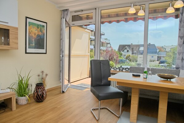 A modern room with a wooden dining table, a black chair, and a large window offering a view of the neighborhood.