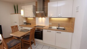 A modern kitchen with white cabinets, a wooden countertop, a built-in oven, and a stainless steel sink. - House Seerose App. 2 incl. WLAN (Grömitz)