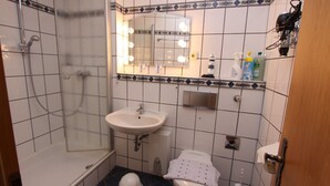A bathroom with a shower, sink, toilet, and a mirror with lights. - House Seerose App. 2 incl. WLAN (Grömitz)