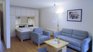 A modern, well-lit room with a bed, two grey armchairs, a grey sofa, a wooden coffee table, and a white wardrobe. - House Seerose App. 2 incl. WLAN (Grömitz)
