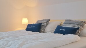 A neatly made bed with white bedding and two blue pillows with text. - House Seerose App. 7 incl. WLAN (Grömitz)