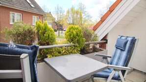 A patio with a table and two chairs, a view of a residential street, and a brick house in the background. - House Seerose App. 7 incl. WLAN (Grömitz)