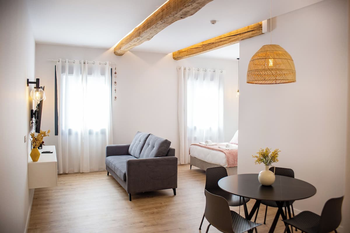 A modern living room with a sofa, a dining table with chairs, and a bed with a white headboard.