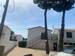 A residential building with a staircase leading to a door, surrounded by trees and a clear sky. - Charming Apartment Near Beach & Shops, La Tranche-sur-Mer (La Tranche-sur-Mer)