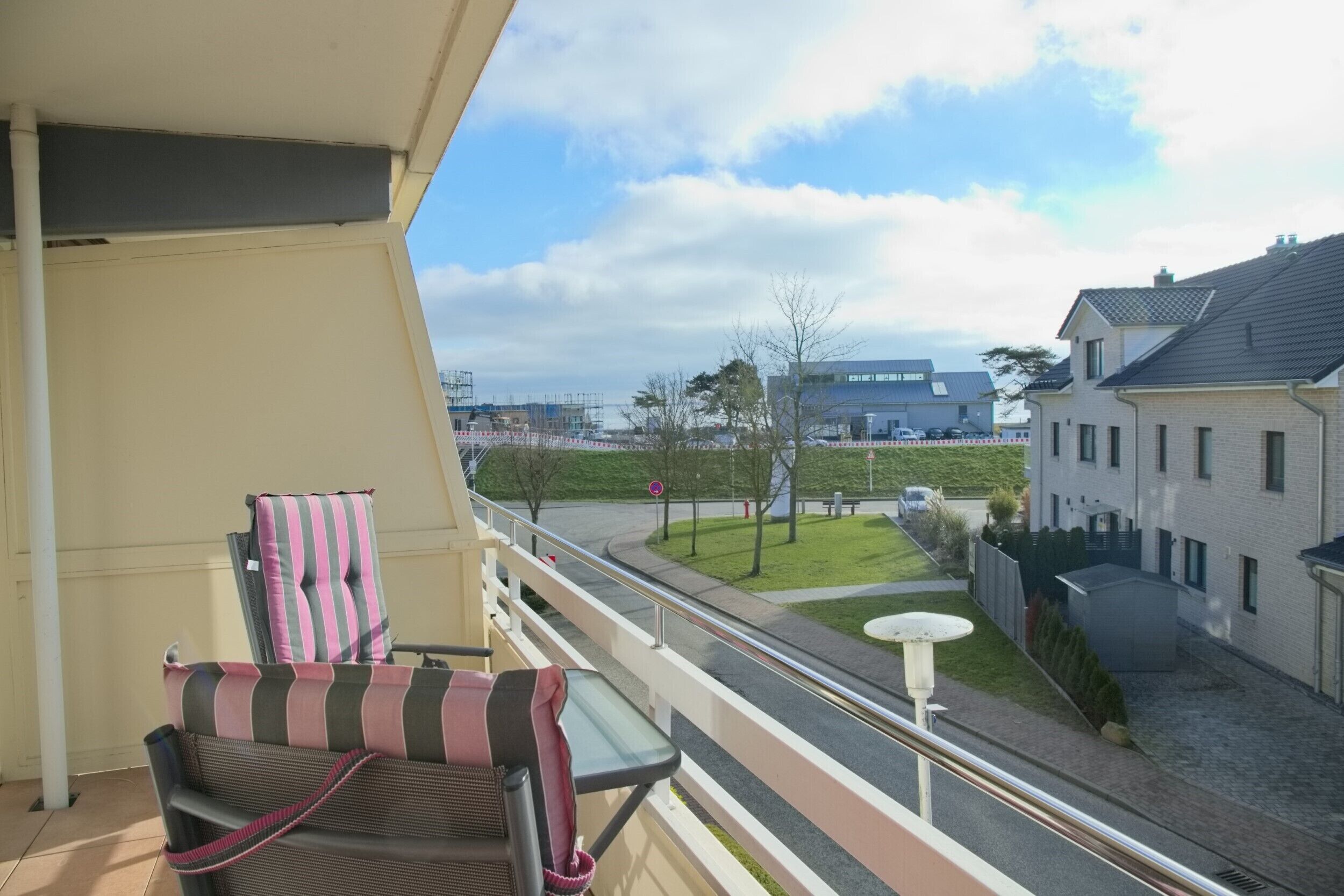 A balcony with a chair and table, overlooking a street with buildings and a clear sky.