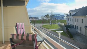 A balcony with a chair and table, overlooking a street with buildings and a clear sky. - House Belvedere App. 23 WLAN incl. (Grömitz)