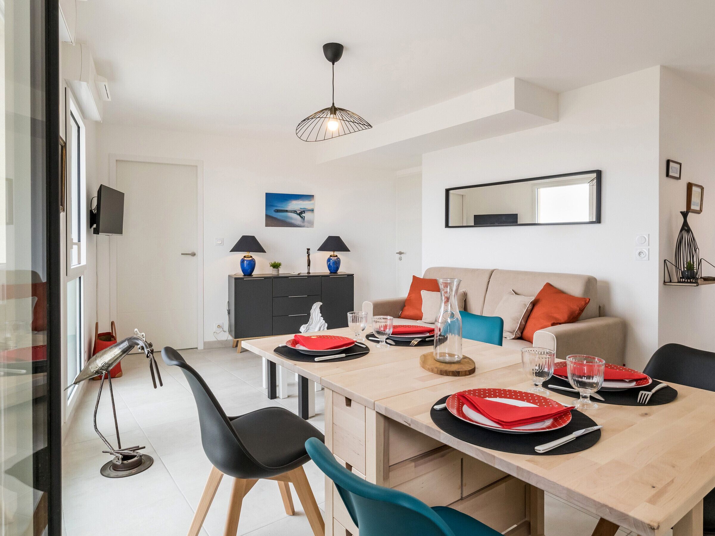 Un coin repas avec une table en bois dressée pour quatre personnes, des chaises noires, un meuble noir et gris, et une suspension.