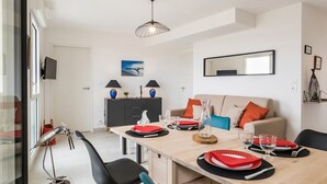 Comedor con mesa de madera dispuesta para cuatro, sillas negras, un armario negro y gris, y una lámpara colgante.