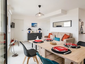 Un coin repas avec une table en bois dressée pour quatre personnes, des chaises noires, un meuble noir et gris, et une suspension.