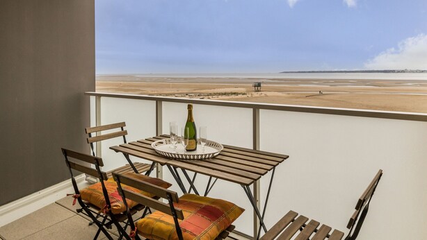 Un balcón con una mesa lista para dos personas, con vista a la playa.