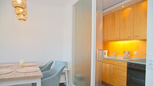 A modern kitchen with wooden cabinets, a built-in oven, and a dining area with a table and chairs. - House Belvedere App. 44 WiFi incl. (Grömitz)