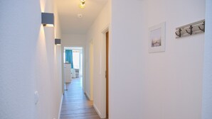 A narrow hallway with white walls and wooden flooring, leading to a room with a door and a window. - House Belvedere App. 44 WiFi incl. (Grömitz)