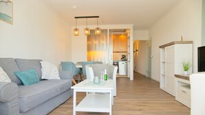 A modern living room with a grey sofa, white coffee table, and a dining area with a table and chairs. - House Belvedere App. 44 WiFi incl. (Grömitz)