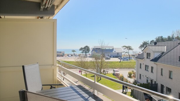 A balcony with a table and chairs, overlooking a parking area and buildings. - House Belvedere App. 44 WiFi incl. (Grömitz)