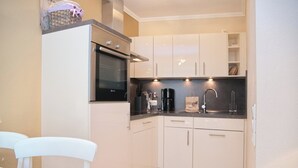 A compact kitchen with white cabinets, a black countertop, and a built-in oven. - Hanseat II App. 137 (Grömitz)