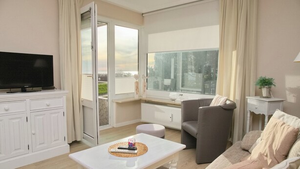 A living room with a television, a sofa, a coffee table, and a large window with curtains. - Hanseat II App. 137 (Grömitz)