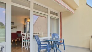 Une terrasse avec une table ronde et des chaises bleues, un canapé rouge et une porte vitrée donnant sur un espace intérieur.