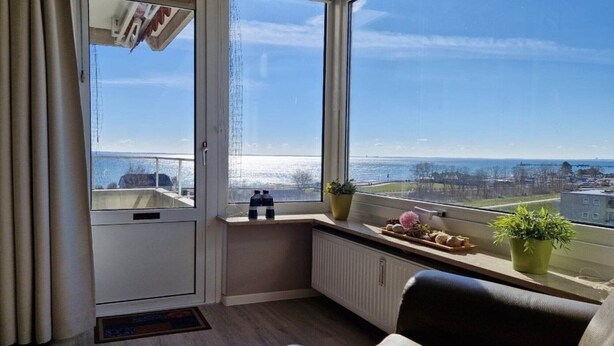 A room with a view of the sea, a radiator, a chair, and a window with a curtain. - Hanseat I Appartement. 82 (Grömitz)