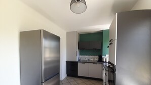 A compact kitchen with stainless steel appliances, a tiled floor, and a green accent wall. - Charming T3 in La Roche-Posay Center with Garden, Garage, and Modern Amenities (La Roche-Posay)