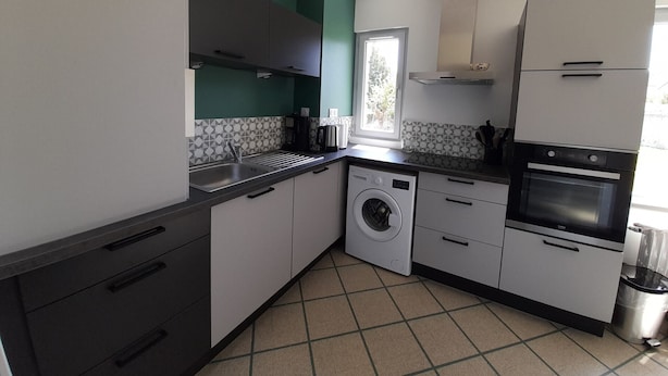 A compact kitchen with a washing machine, oven, and a window providing natural light. - Charming T3 in La Roche-Posay Center with Garden, Garage, and Modern Amenities (La Roche-Posay)