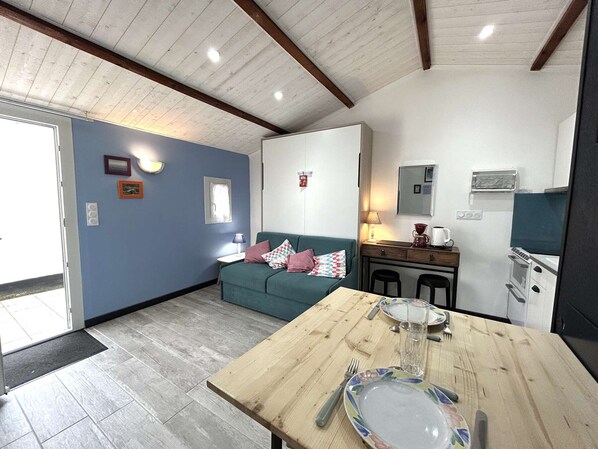 A cozy living area with a wooden table set for dining, a blue sofa, and a kitchenette with a microwave and stove.