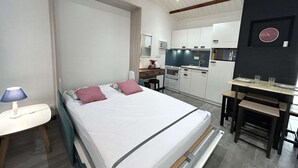 Un dormitorio con cama, mesita de noche y un pequeño escritorio con silla. Cuenta con una kitchenette equipada con estufa, horno y microondas.
