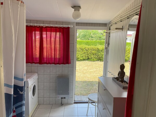 A laundry room with a washing machine, a dryer, a radiator, and a small table. - Freistehender Bungalow mit Garten Fußläufig zum Strand (Ouddorp)