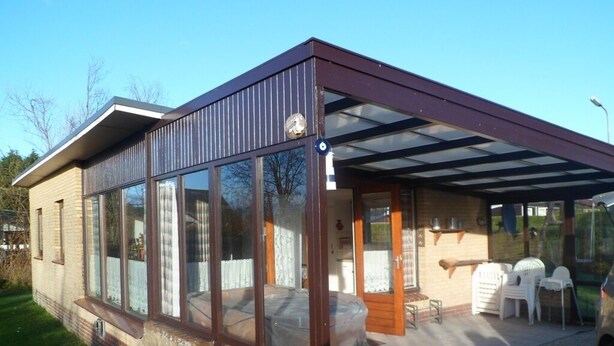 A modern house with large windows, a covered patio, and a small outdoor seating area.