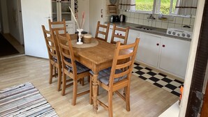 A kitchen with a wooden dining table, chairs, a stove, and a window with curtains.