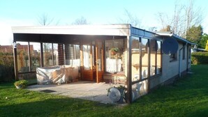 A covered outdoor area with a wooden deck, a seating area, and a large windowed section.
