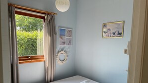 A bedroom with a bed, a window with curtains, a wall-mounted light fixture, and a framed picture.