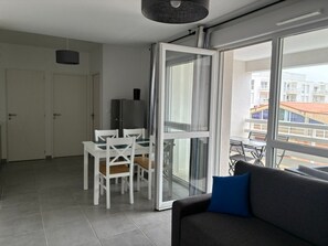 A modern living room with a grey sofa, a dining table with chairs, a TV, and a large sliding glass door leading to a balcony. - Beautiful air-conditioned T2 for 4 with parking, near beach in Port Leucate (Port Leucate)