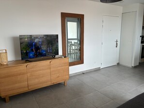 Uma sala de estar moderna com uma televisão de tela plana em um móvel de madeira, uma porta branca e vista para uma varanda externa.