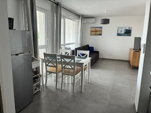 A modern kitchen with a refrigerator, dining table with chairs, and a sofa in the living area.