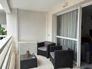 A balcony with a white railing, a black outdoor seating area with two chairs and a small table, and a sliding glass door leading to an interior room.