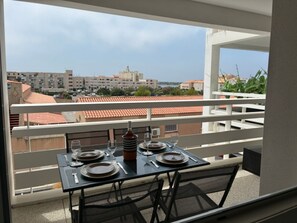 A balcony with a table set for two, overlooking a cityscape with buildings and a clear sky. - Beautiful air-conditioned T2 for 4 with parking, near beach in Port Leucate (Port Leucate)