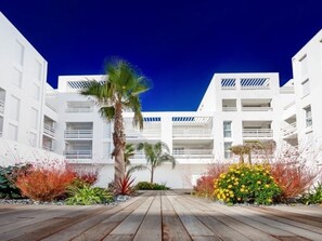 Stunning hotel facade with white balconies and a flat roof, surrounded by a deck and lush garden.