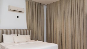 Une chambre d’hôtel avec un lit, des rideaux beiges, un appareil de climatisation et un interrupteur.