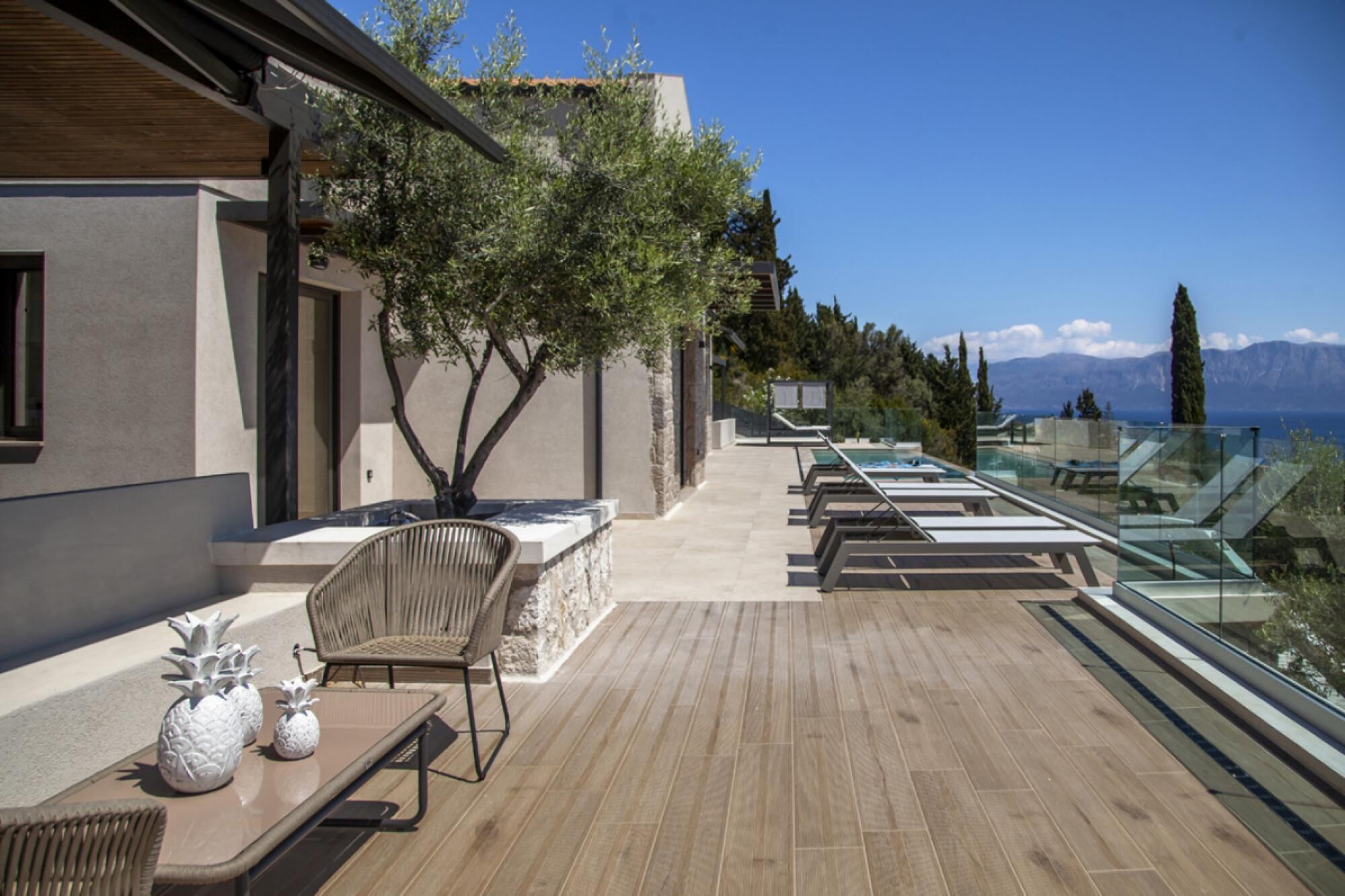 A modern outdoor terrace with a pool, lounge chairs, and a view of mountains.