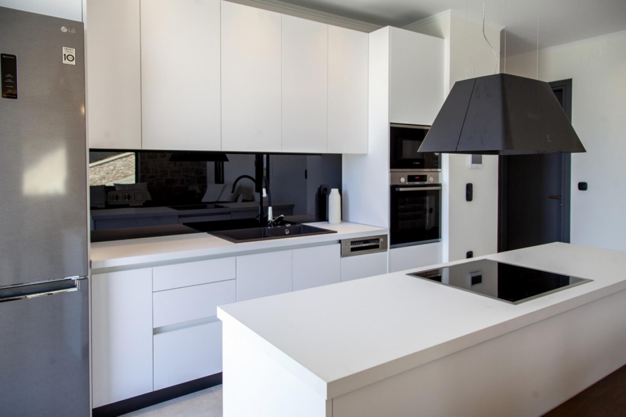 Une cuisine moderne avec des meubles blancs, un plan de travail noir et un four encastré.