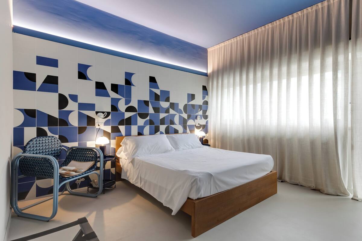 Un dormitorio moderno con una cama de madera, una silla azul y un diseño geométrico en la pared.