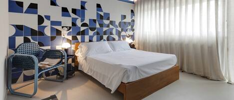 A modern bedroom with a wooden bed, a blue chair, and a geometric wall design.