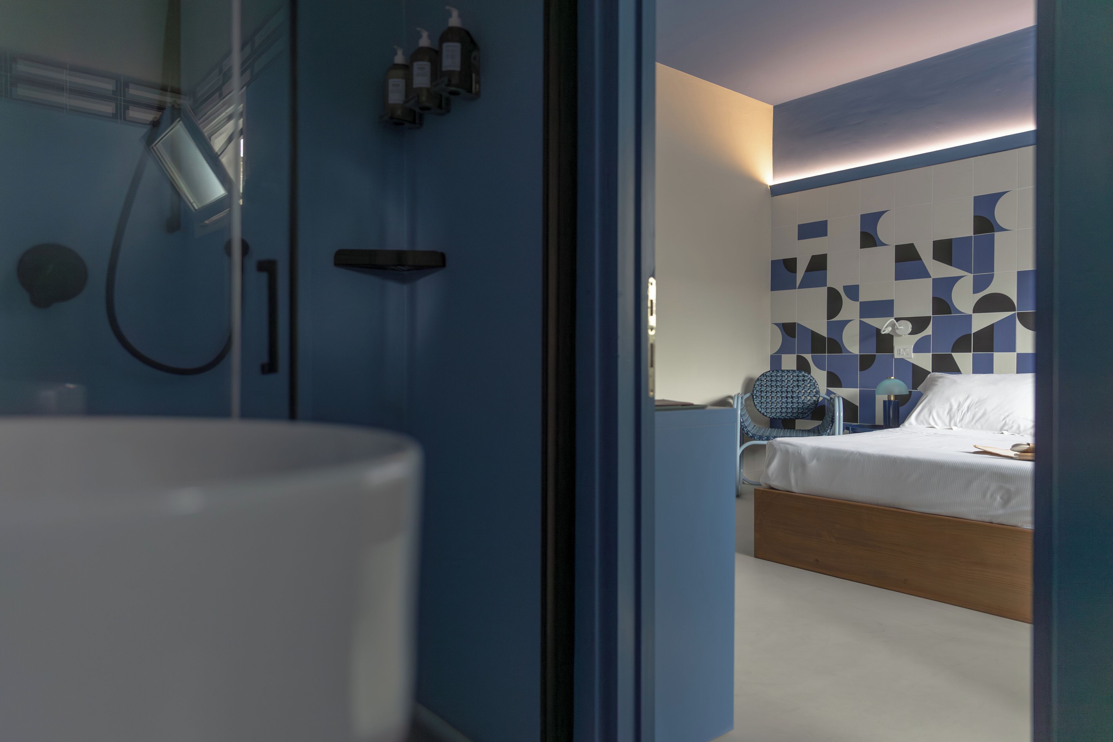 A modern bathroom with a shower, a sink, and a mirror. The room has a blue accent wall and a bed with a white mattress and wooden headboard.