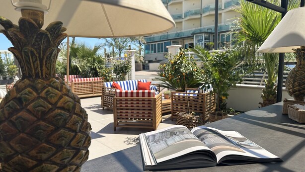 An outdoor seating area with wicker furniture, a pineapple sculpture, and an open magazine on a table. - MARITTIMO® Milano Marittima (Cervia)