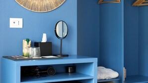 A blue room with a round mirror, a small shelf with a tissue box, glasses, and a bottle. - MARITTIMO® Milano Marittima (Cervia)