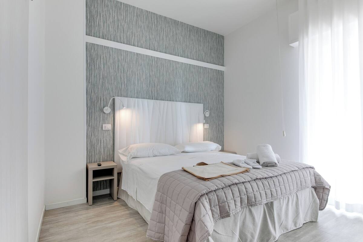 Un dormitorio moderno con una cama grande, mesitas de noche y una paleta de colores neutros.