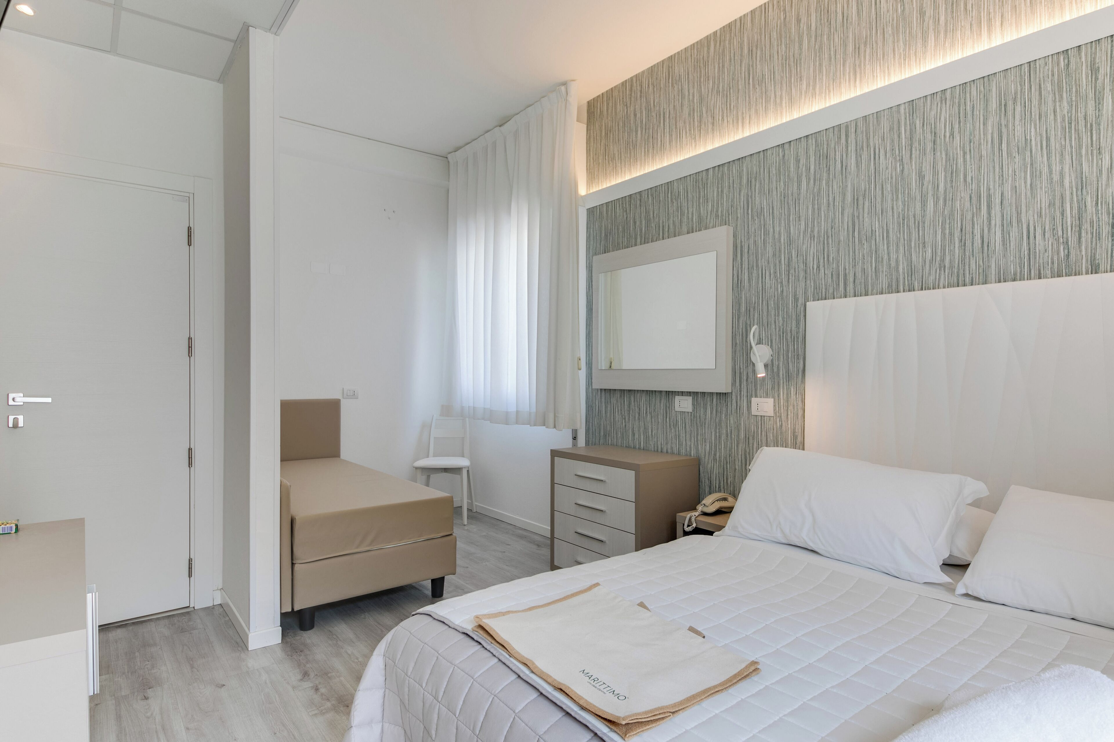 A modern bedroom with a bed, bedside table, and a mirror.