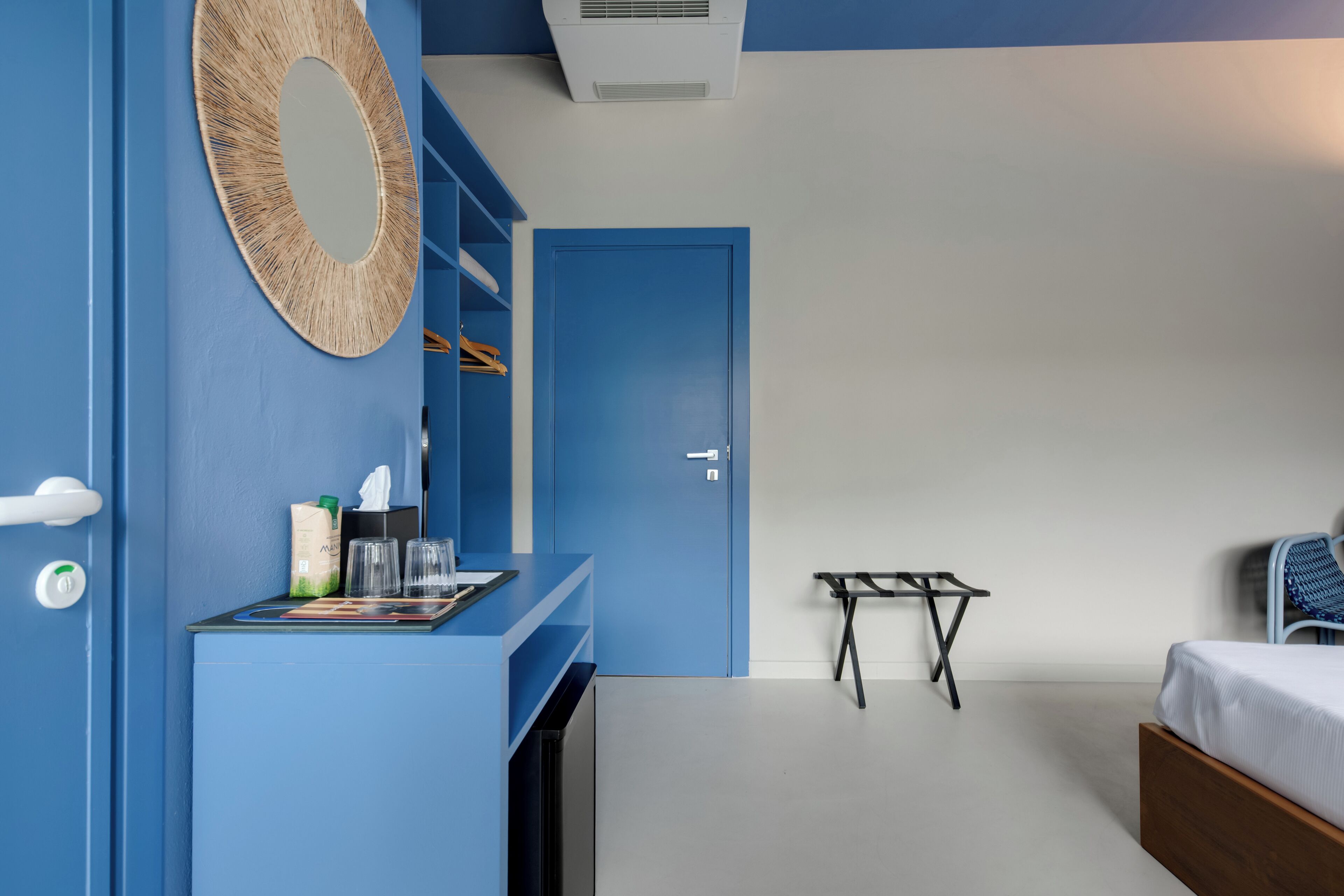 A room with a blue door, a bed, a small table, and a mirror on the wall.