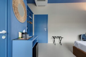 Una habitación con puerta azul, una cama, una mesita y un espejo en la pared.